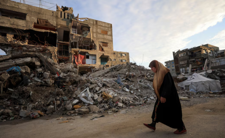 ഗാസ യുദ്ധത്തിൽ തകർന്ന കെട്ടിടങ്ങൾക്കരികിലൂടെ നടക്കുന്ന പലസ്തീൻ വനിത